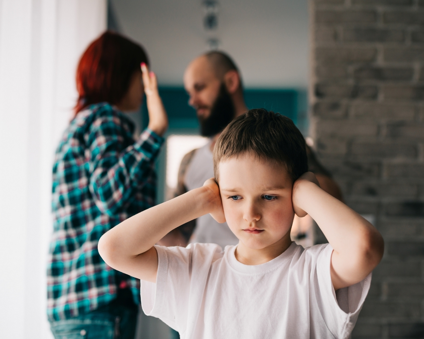 En gutt holder seg for ørene. Bak ham ser man en mann og en kvinne som krangler.